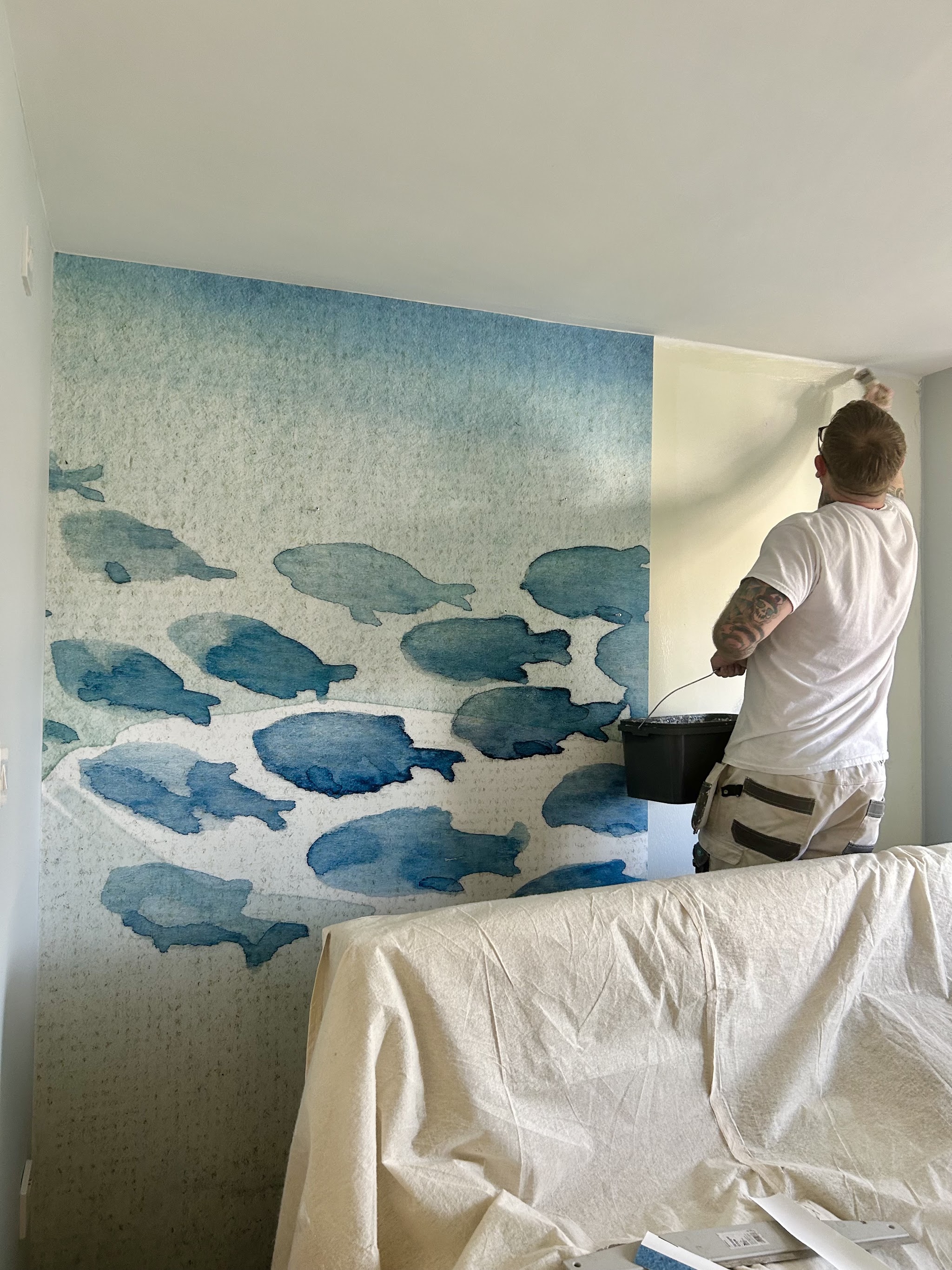 Jay hanging a watercolour fish feature wallpaper on a bedroom wall
